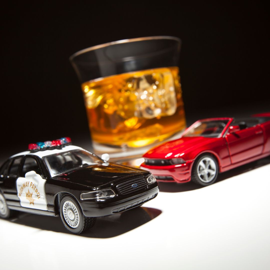 Toy cars surrounding a glass of alcohol. 